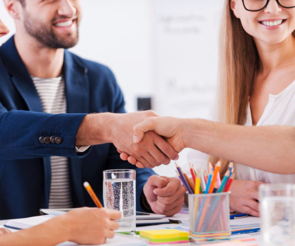 Congratulations! Close-up of business people in smart casual wear shaking hands and smiling while sitting at the table together